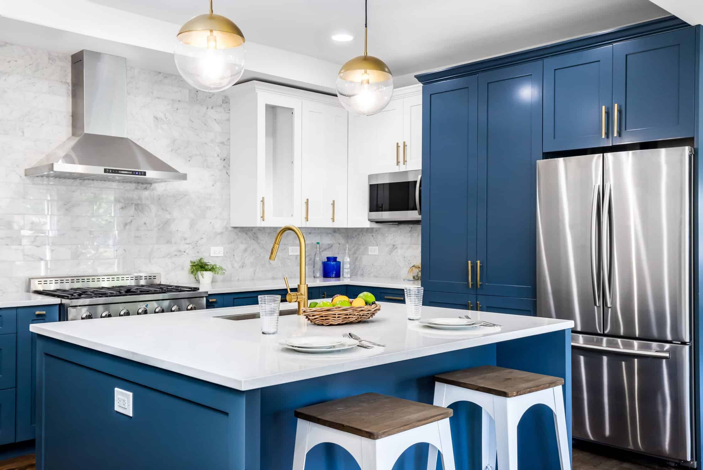 Navy Blue Kitchen Cabinet Remodel Navy blue painted kitchen cabinetry with white island, marble backsplash, brass hardware, and stainless steel appliances.