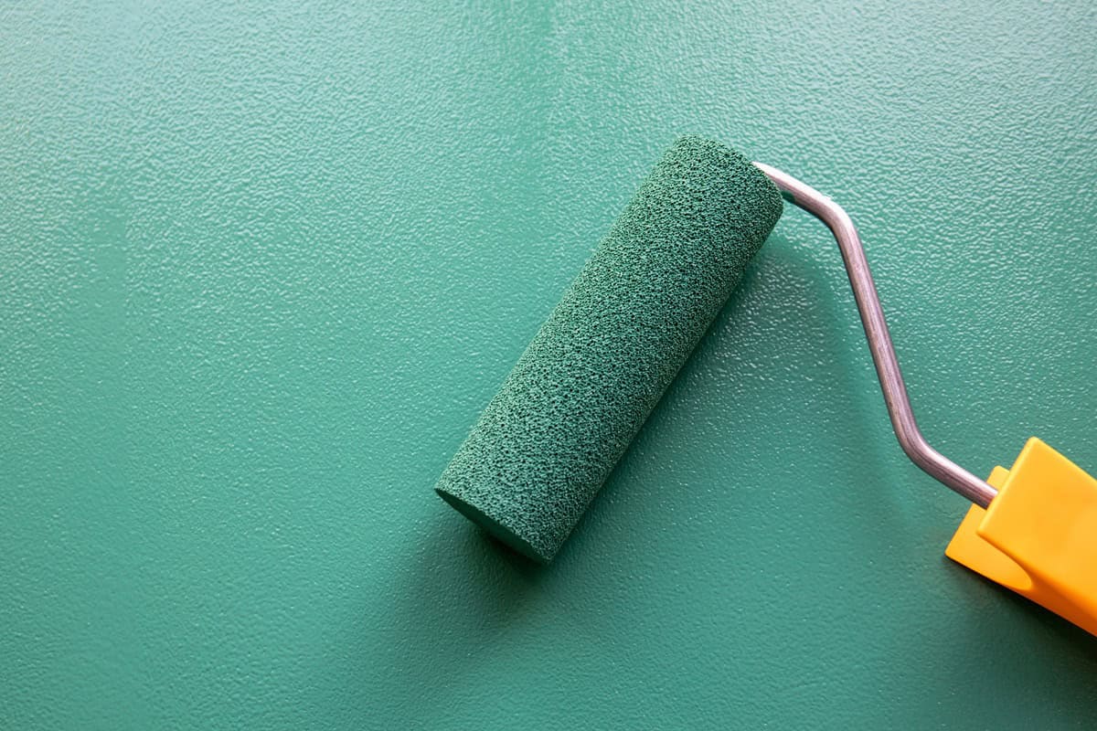 Paint roller with green colour on painted wooden surface. Chalk board