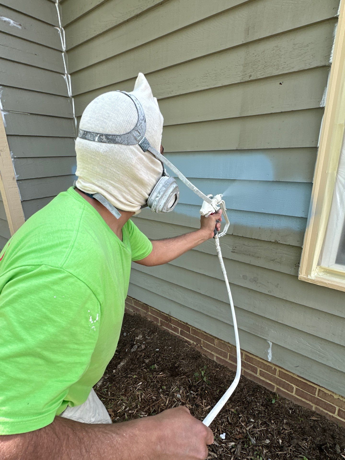 Expert painter spray painting house exterior siding A professional painter in protective gear spray paints light blue siding on a house exterior.
