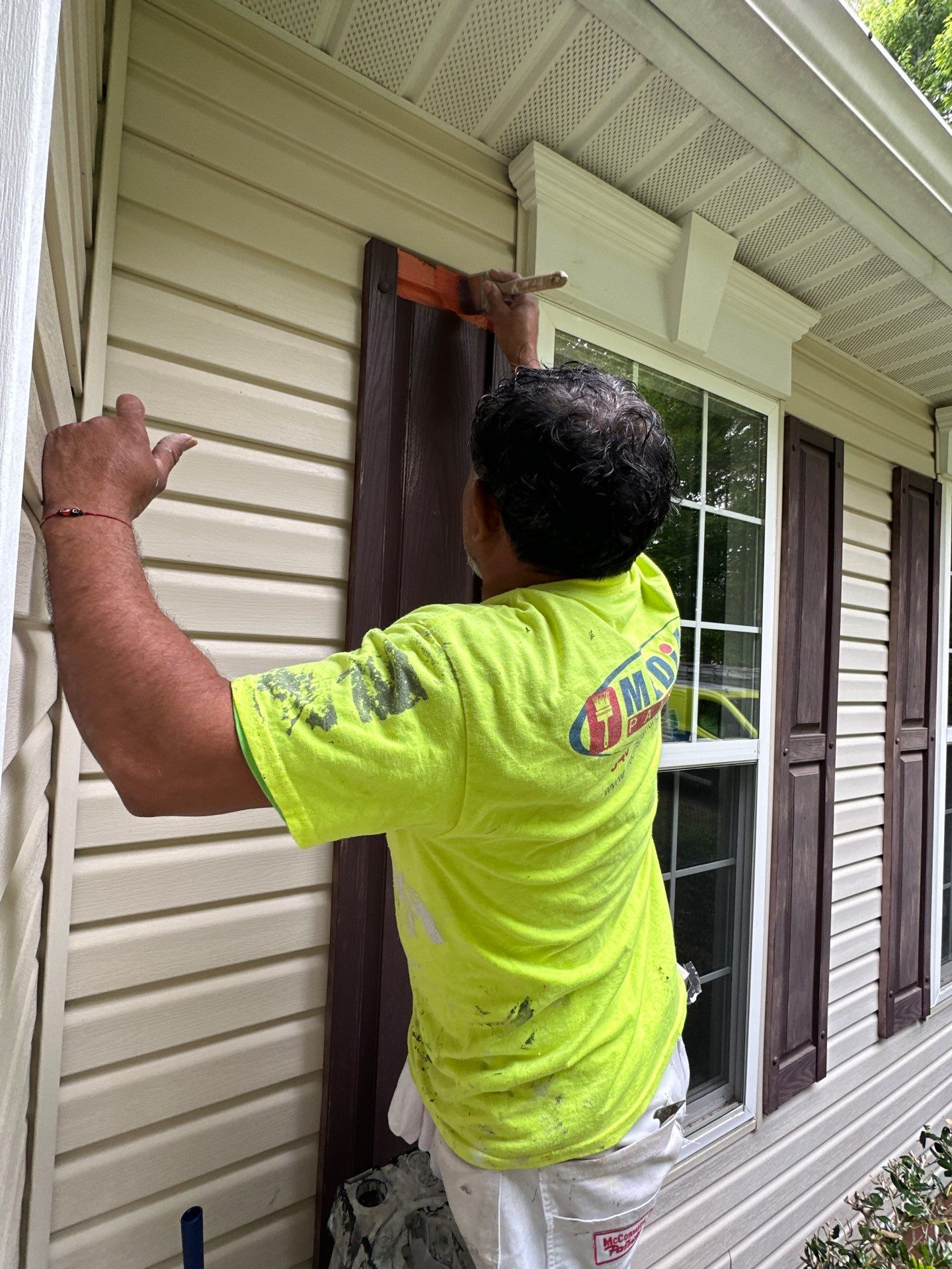 A professional painter from Medias Painting uses a brush to paint exterior house shutters orange.
