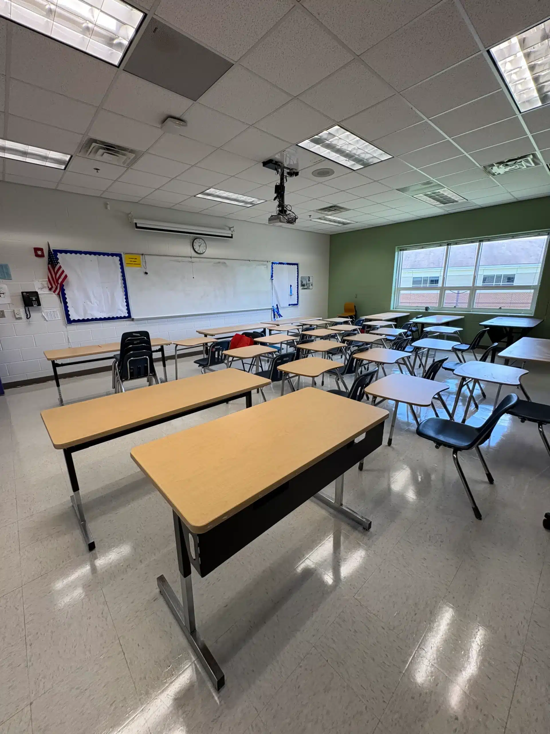 Classroom Interior Painting Project Bright classroom with white ceiling tiles, green accent wall, white and blue whiteboards, student desks, and fluorescent